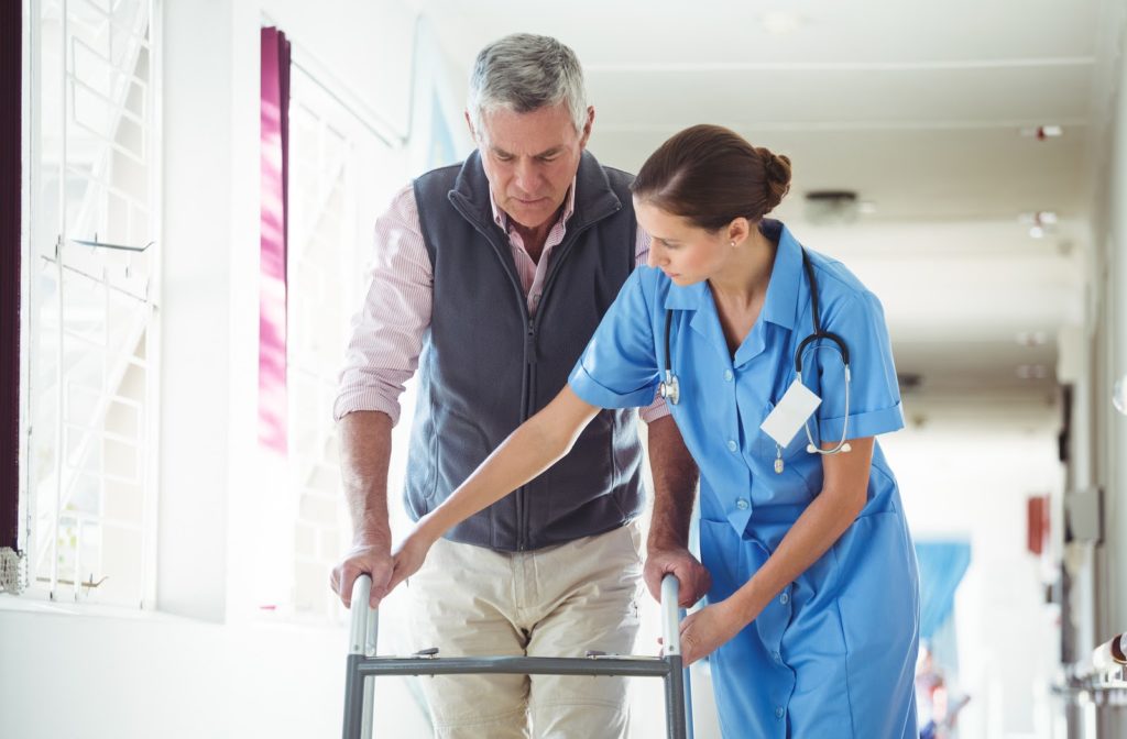 Nurse at senior community helping senior gentleman walk across the hall.