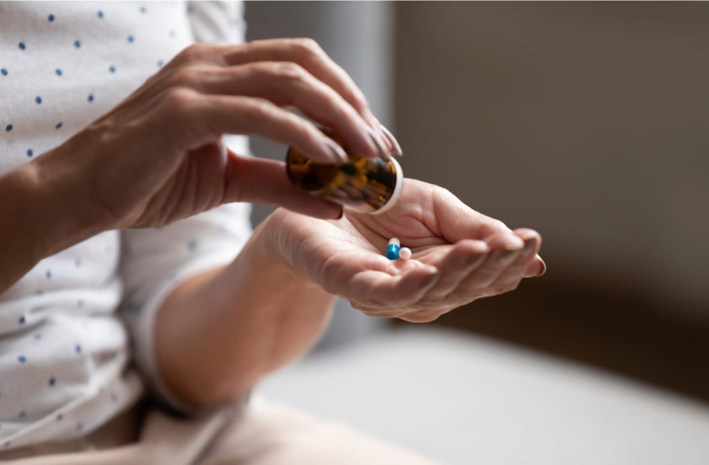 Senior woman taking medication as she puts the pills in her hands from container.