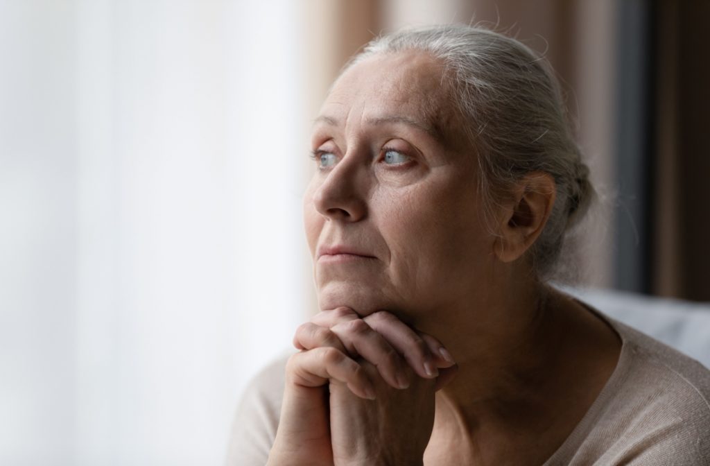 Thoughtful-looking senior woman rests chin on her clasped hands.