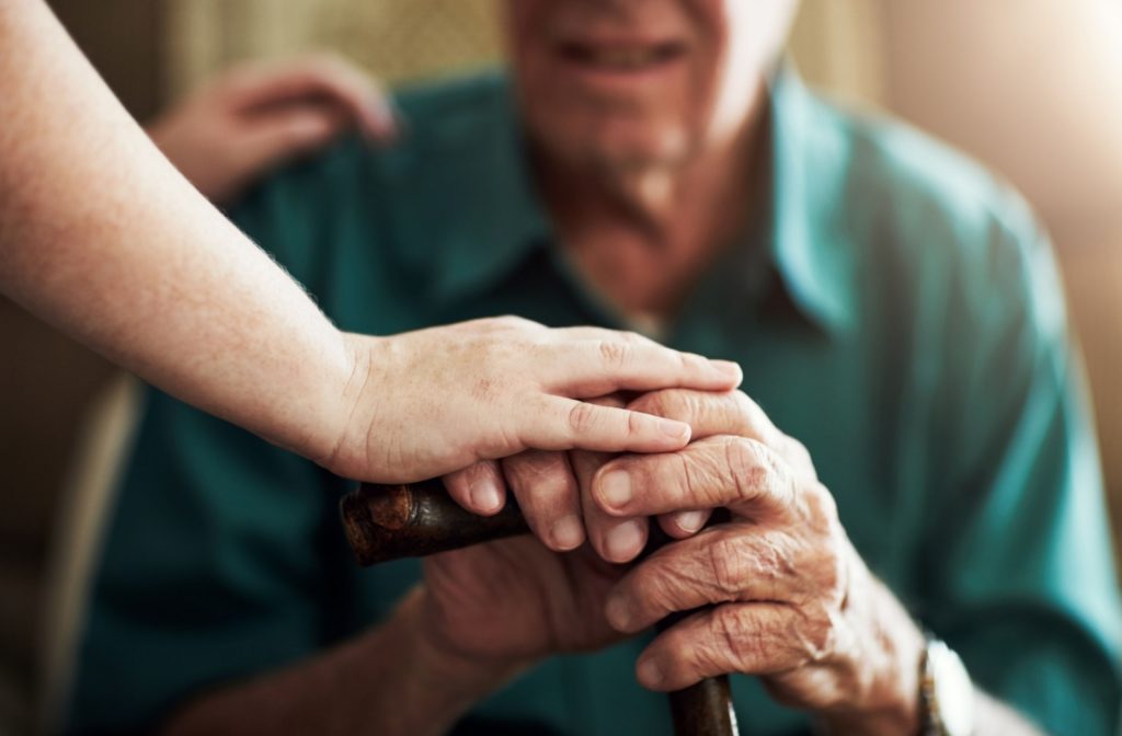 Close up of a person holding hands with a senior, holding a cane.